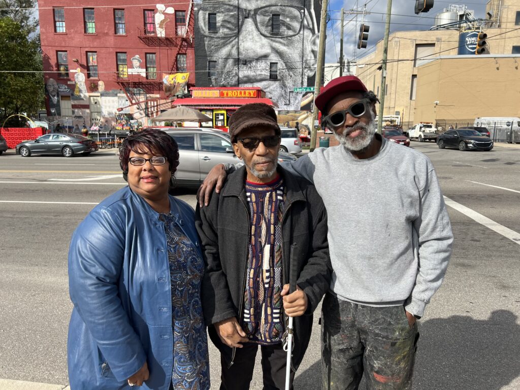 Artist Chip Thomas with William Rankins Jr. and his case manager Deb Clinkscale standing in front of the mural at Ollie's Trolley.